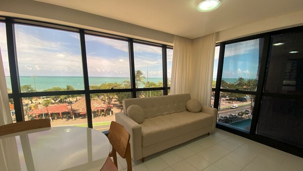 A spacious room with a large window offering a view of the beach and ocean. - Edificio Neo Apto 401-Mandi H (Maceio)