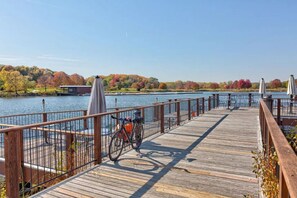 A wooden pier with a bicycle and umbrellas, overlooking a lake with autumn foliage.