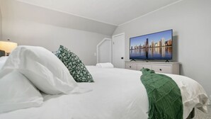 Ein Schlafzimmer mit einem Bett, Kissen, einer grünen Tagesdecke, einem Fernsehgerät an der Wand und einem Nachttisch mit einer Lampe.