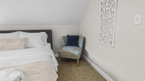 Een slaapkamer met een bed, een gestreept fauteuil en een decoratief wandpaneel.