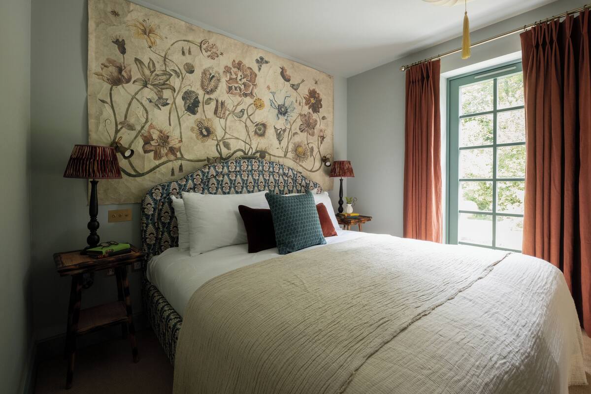 A large bed with a patterned headboard, two bedside tables with lamps, and a window with curtains.
