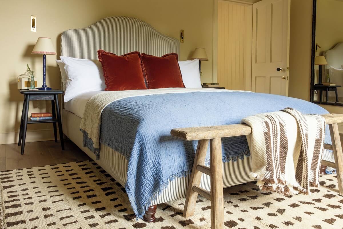 A neatly made bed with a striped headboard, a wooden bench, and a patterned rug.