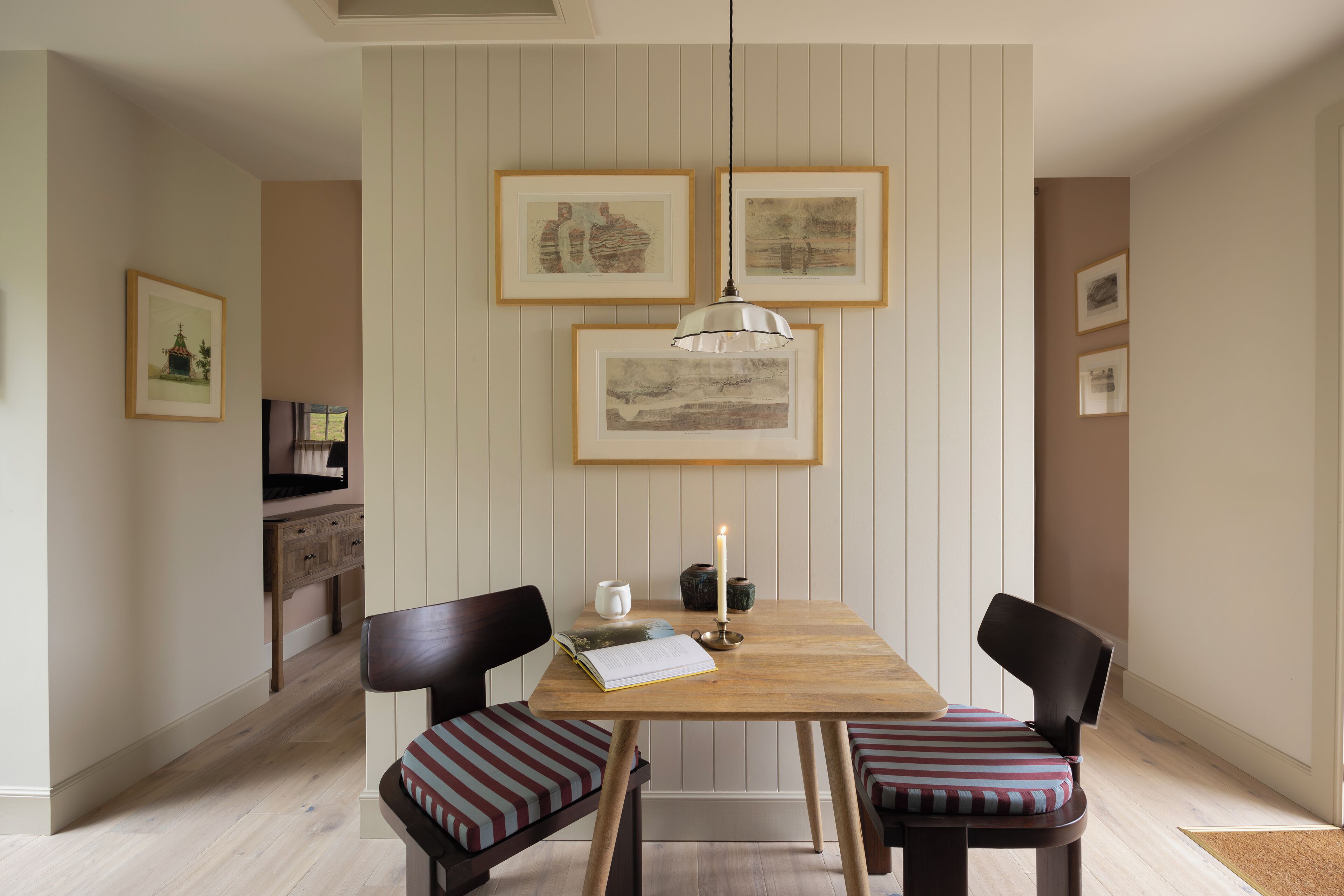 Un área de comedor con una mesa de madera, dos sillas, una lámpara colgante y cuadros en la pared.