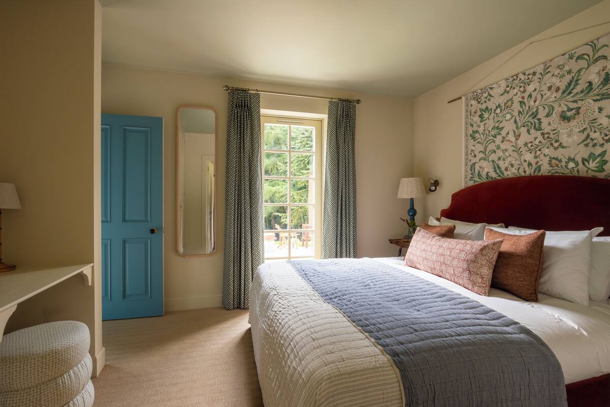A bedroom with a large bed, a blue door, a window with curtains, and a patterned wall.