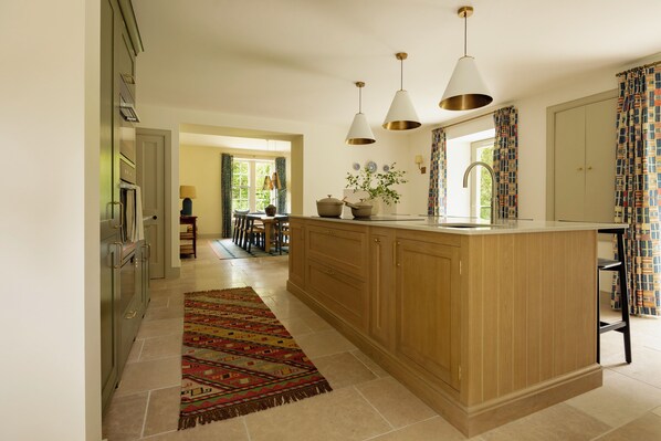 A kitchen with wooden cabinets, a central island, pendant lights, and a patterned rug. - Penicuik Estate (Penicuik)