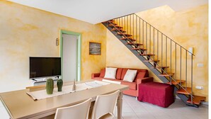 A living room with a sofa, a dining table, a TV, and a staircase. - SkyView Apartment in BOSA (Bosa)