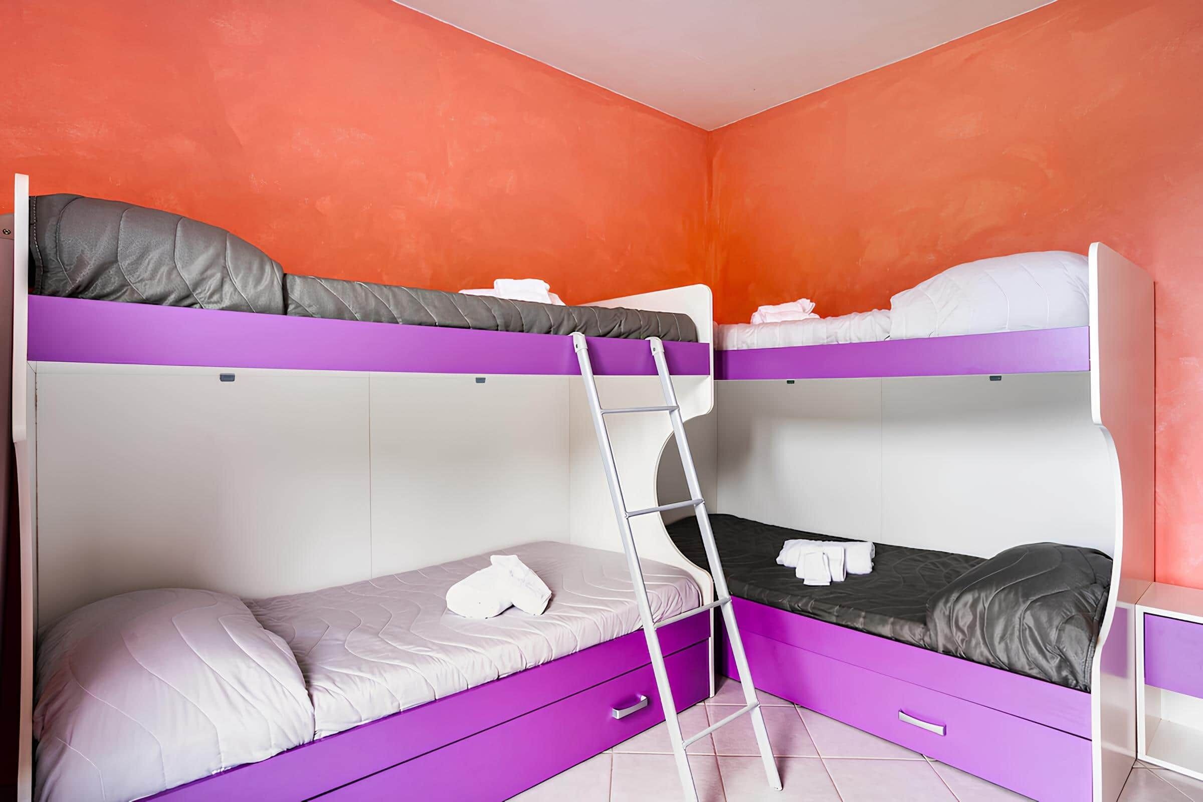 Camera con letto a castello, una scala, un cassetto viola e una parete bianca.