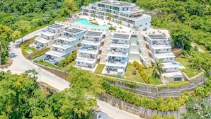 Un complexe hôtelier moderne composé de plusieurs bâtiments, doté d’une piscine centrale et entouré d’une végétation luxuriante.