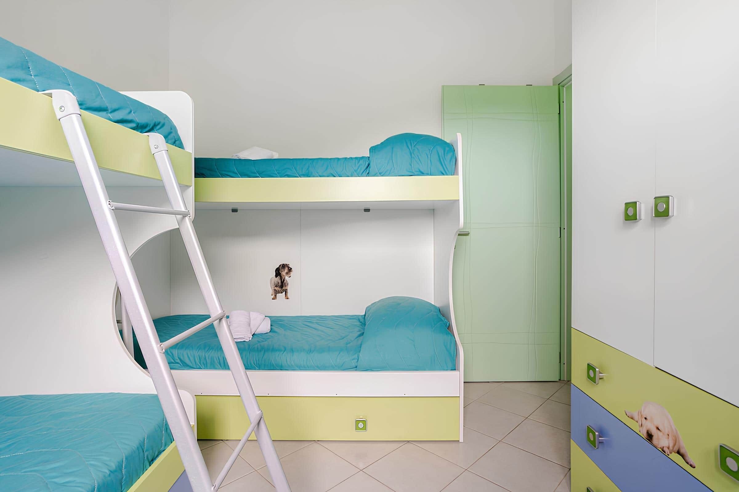 Habitación con literas, una escalera, una puerta verde y un cuadro pequeño en la pared.