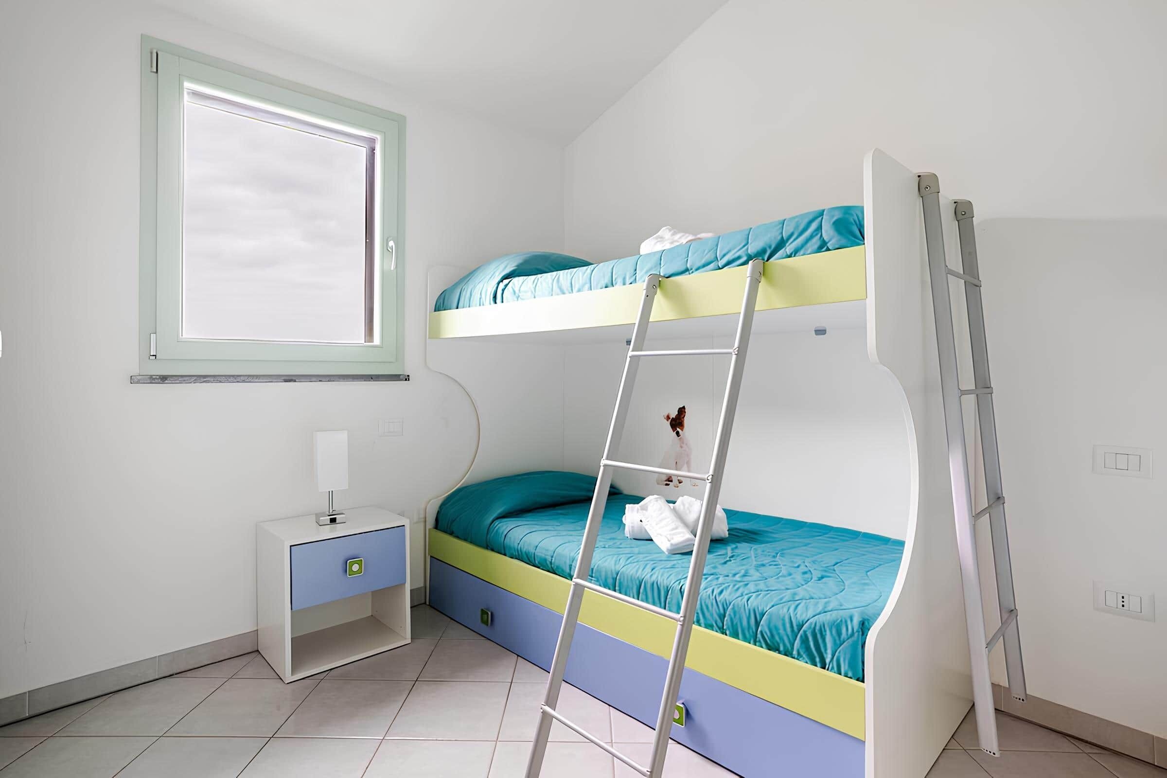 Un letto a castello con una scala, un comodino con una lampada e una finestra.