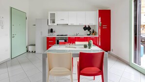 A modern kitchen with white and red cabinetry, a central island with chairs, and a sliding glass door to the right. - Sunset Apartment in BOSA (Bosa)