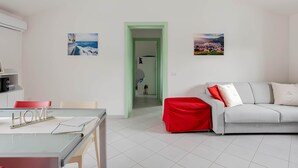 A modern living room with a glass table, a white sofa with red cushions, and two framed pictures on the walls. - Sunset Apartment in BOSA (Bosa)