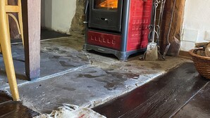 A room with a red wood-burning stove, a wooden table, and a patterned rug on the floor. - Cà Nova 1590, a charming accommodation in an ancient hamlet (Emilia-Romagna)