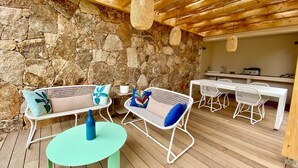 An outdoor patio with wicker furniture, a stone wall, and a wooden ceiling. - Les Bergeries de Figari (Figari)