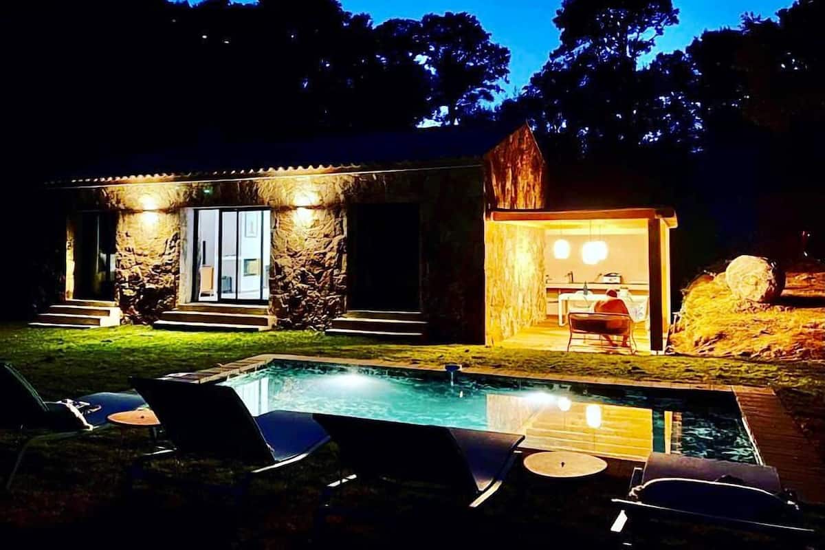 A house with a swimming pool, outdoor seating, and a stone facade.
