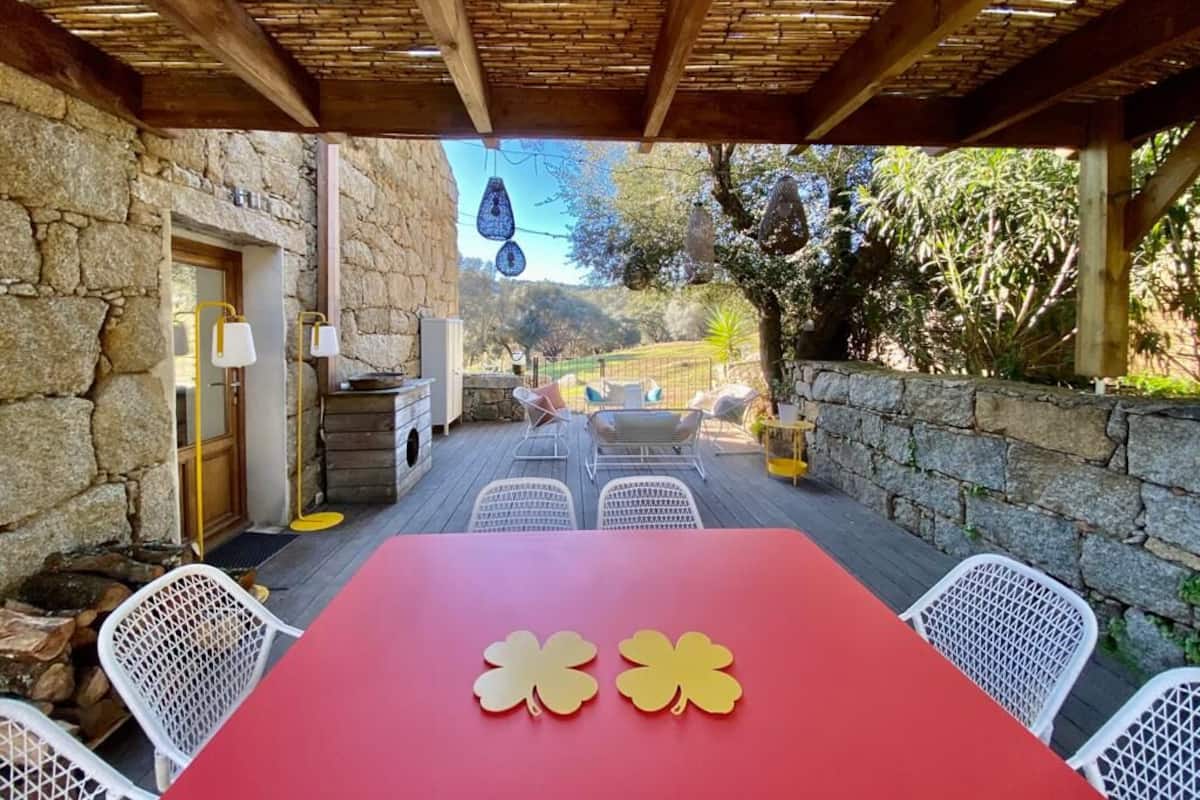 An outdoor patio with stone walls, a red table, and white chairs.