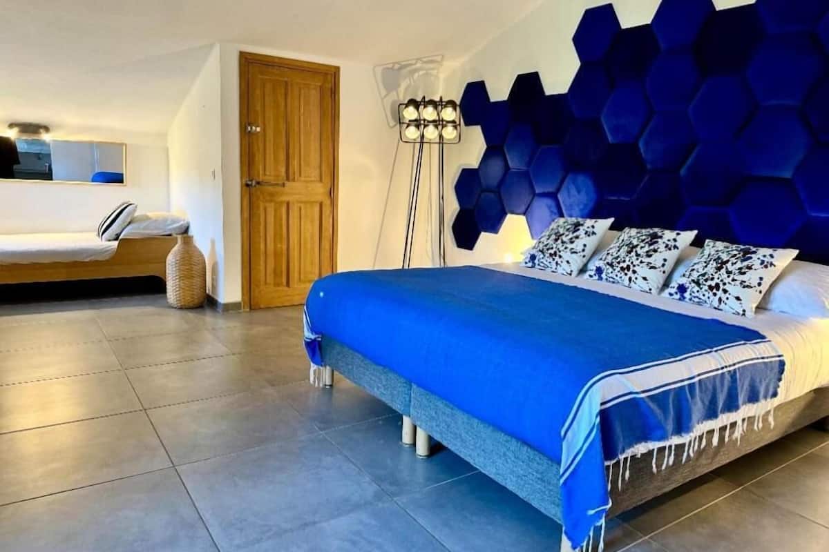 A modern bedroom with a large bed, a wooden door, a floor lamp, and a wall with a geometric pattern.