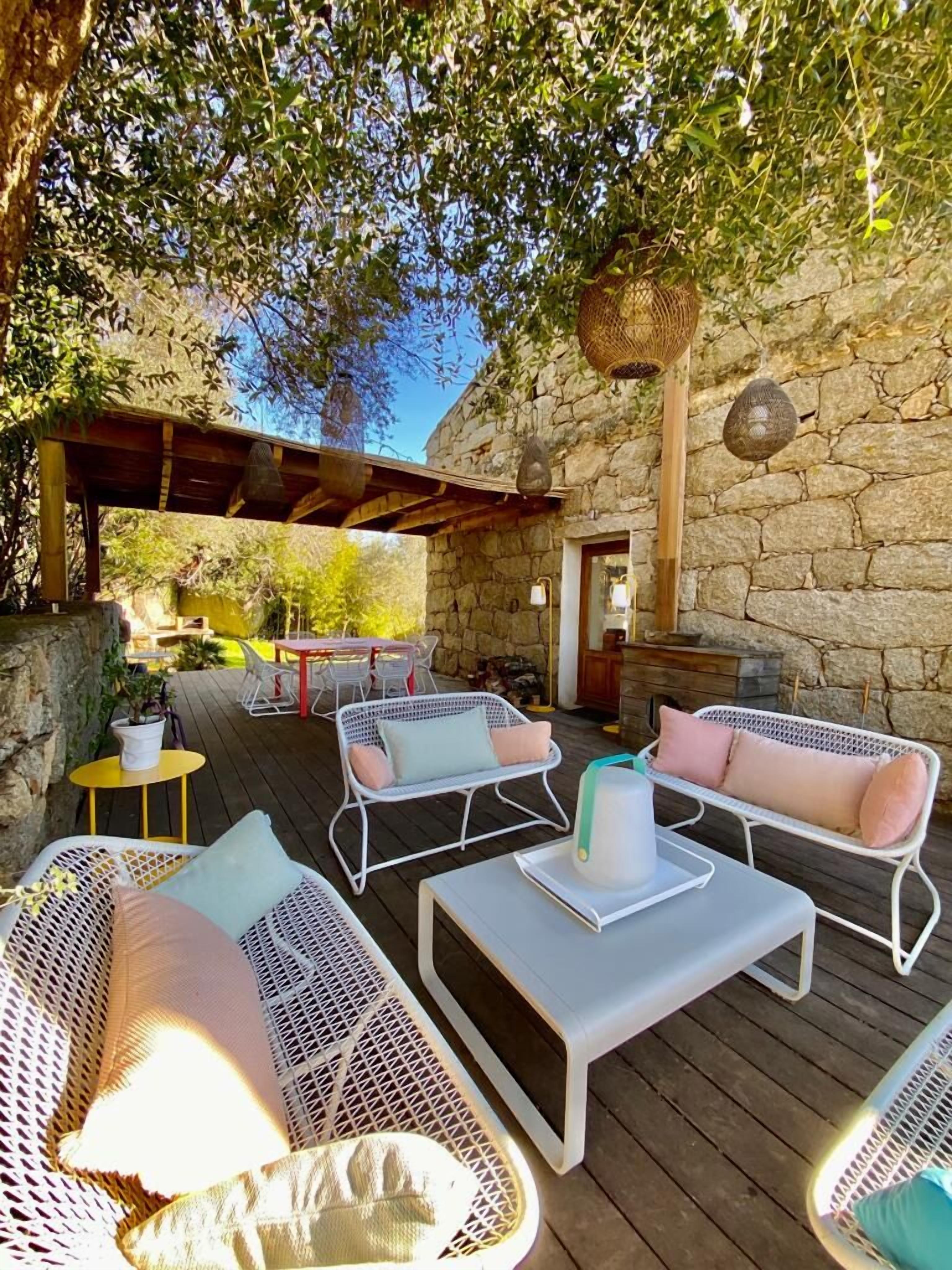 Un patio al aire libre con mobiliario de mimbre, una pared de piedra y una pérgola.