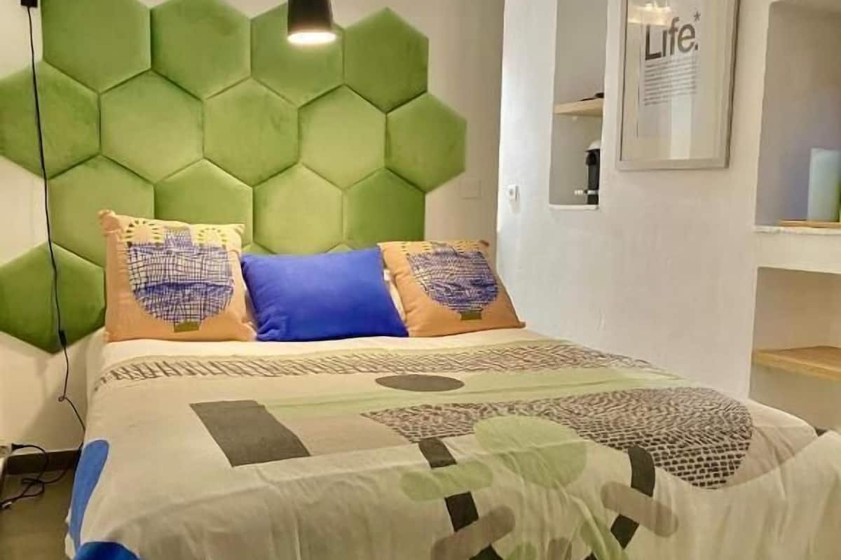 A modern bedroom with a hexagonal green headboard, a patterned bedspread, and a bedside lamp.