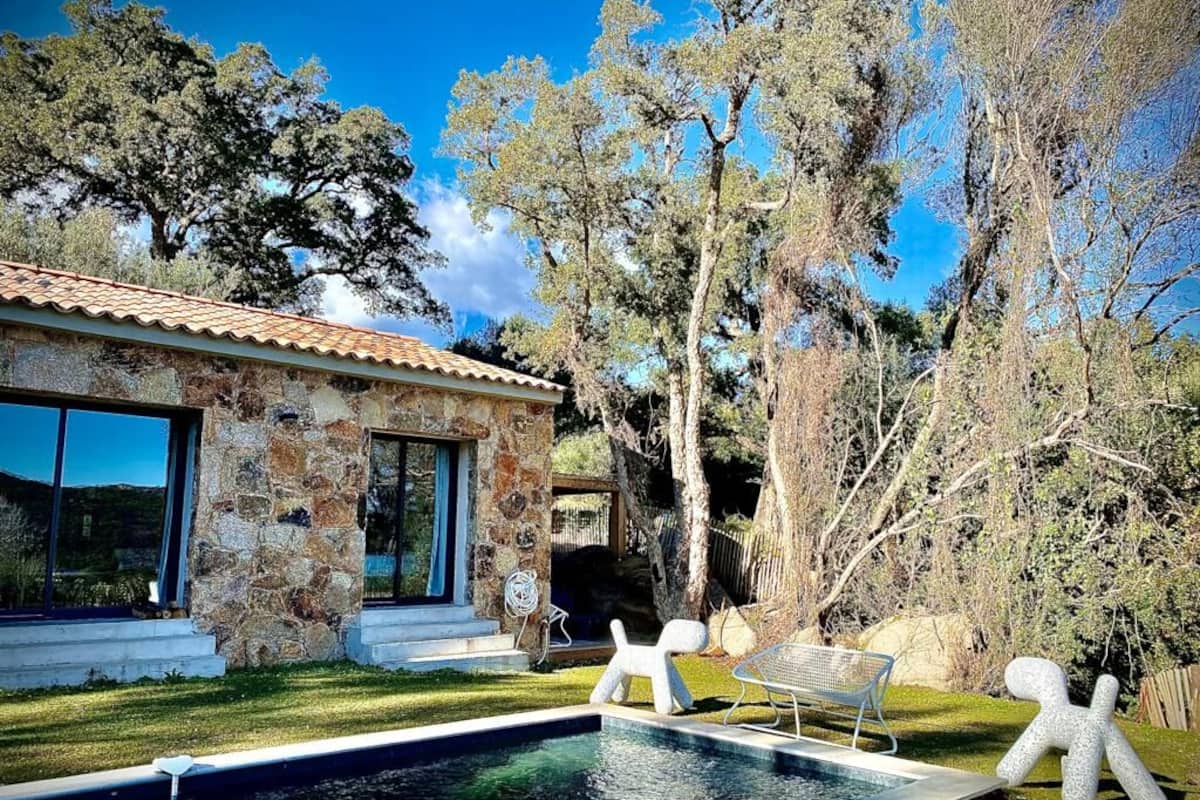 A stone house with a swimming pool, outdoor seating, and trees.
