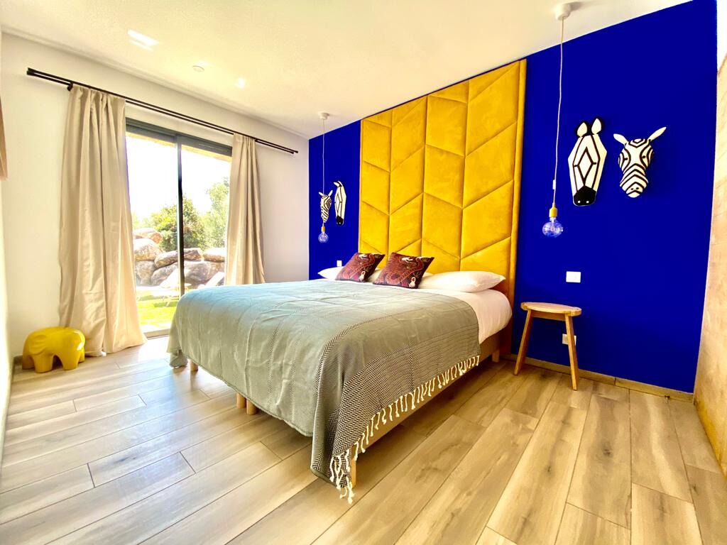 A bedroom with a bed, a small stool, and a window with curtains.