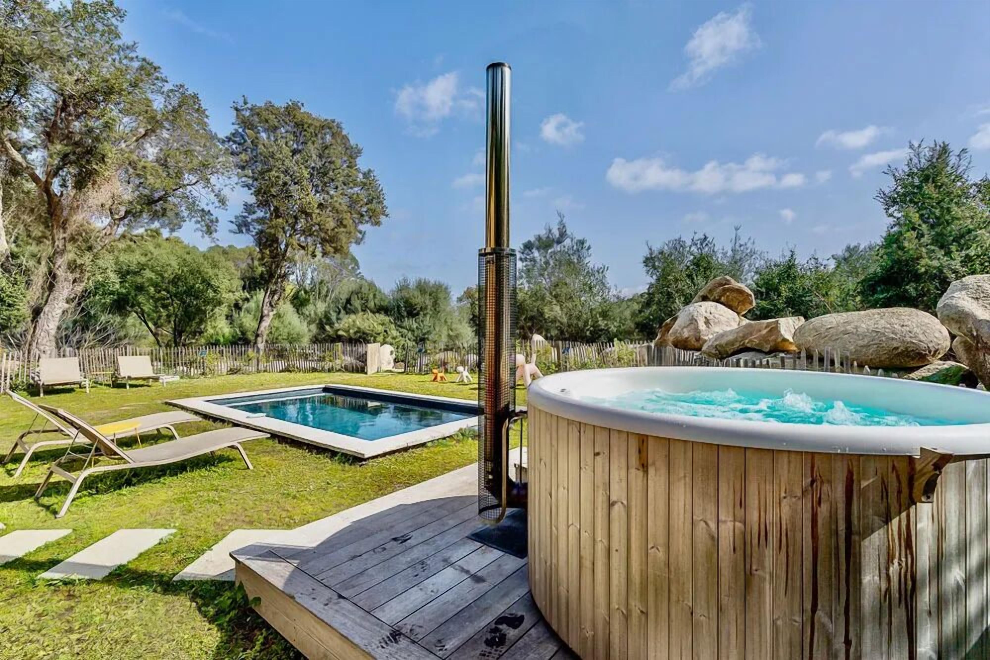 A backyard with a hot tub, a swimming pool, and lounge chairs.