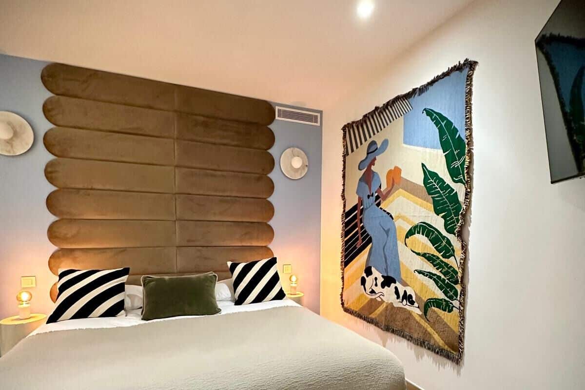 A modern bedroom with a large bed, a unique headboard, a wall-mounted artwork, and a bedside table with a lamp.