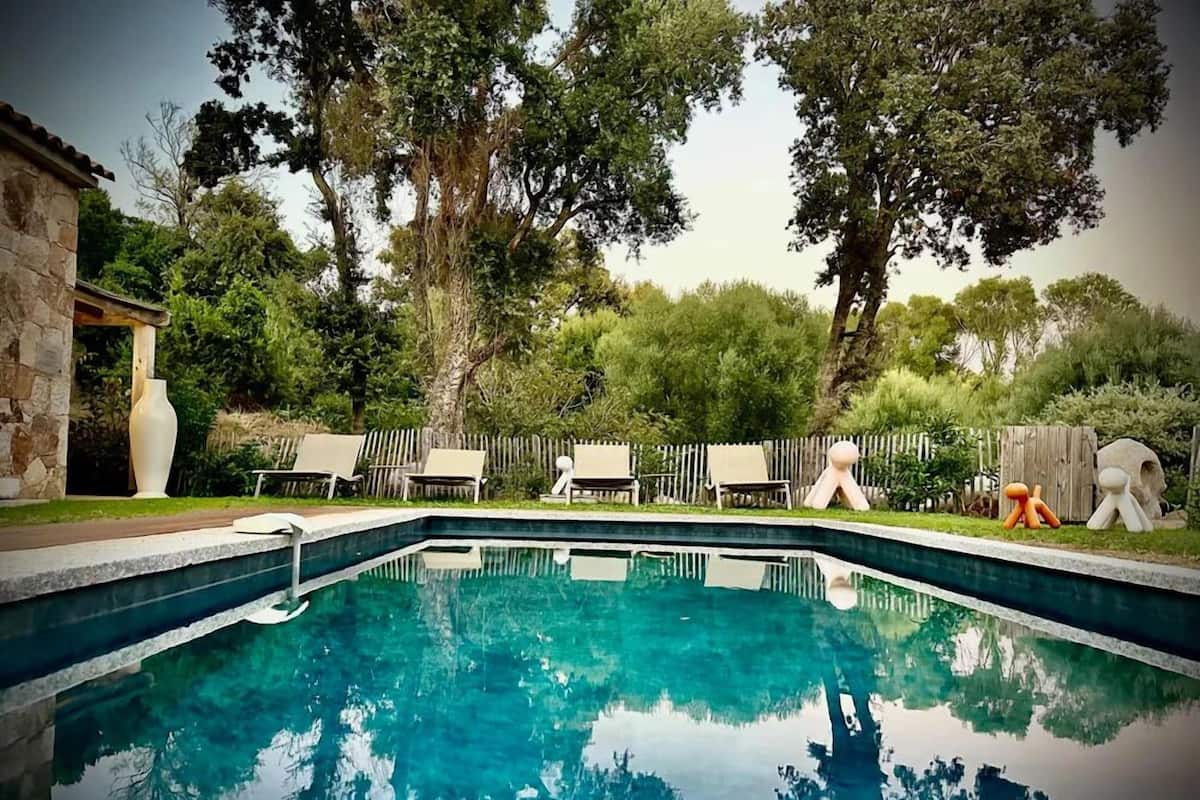 A rectangular swimming pool with clear blue water, surrounded by a stone wall, a wooden deck, and a wooden fence.