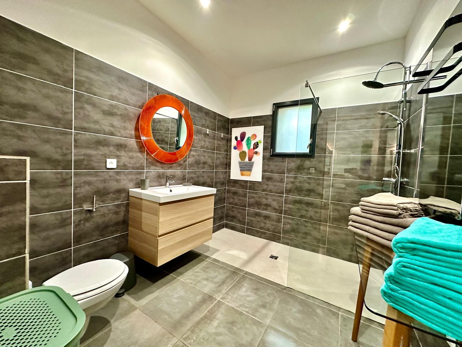 Un baño moderno con tocador de madera, un espejo redondo, ducha e inodoro.