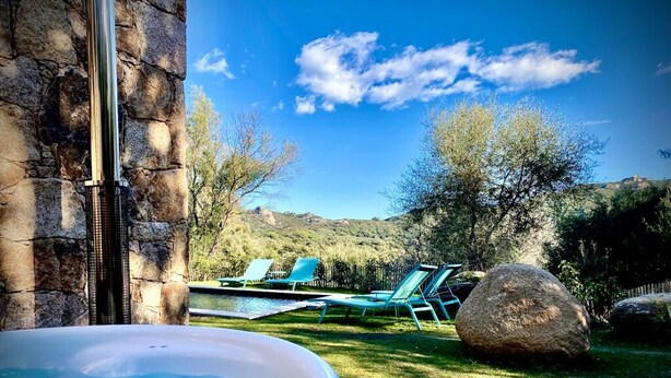 A hot tub in a garden with a stone wall, a pool, and lounge chairs. - Les Bergeries de Figari (Figari)