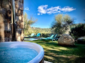 A hot tub in a garden with a stone wall, a pool, and lounge chairs. - Les Bergeries de Figari (Figari)
