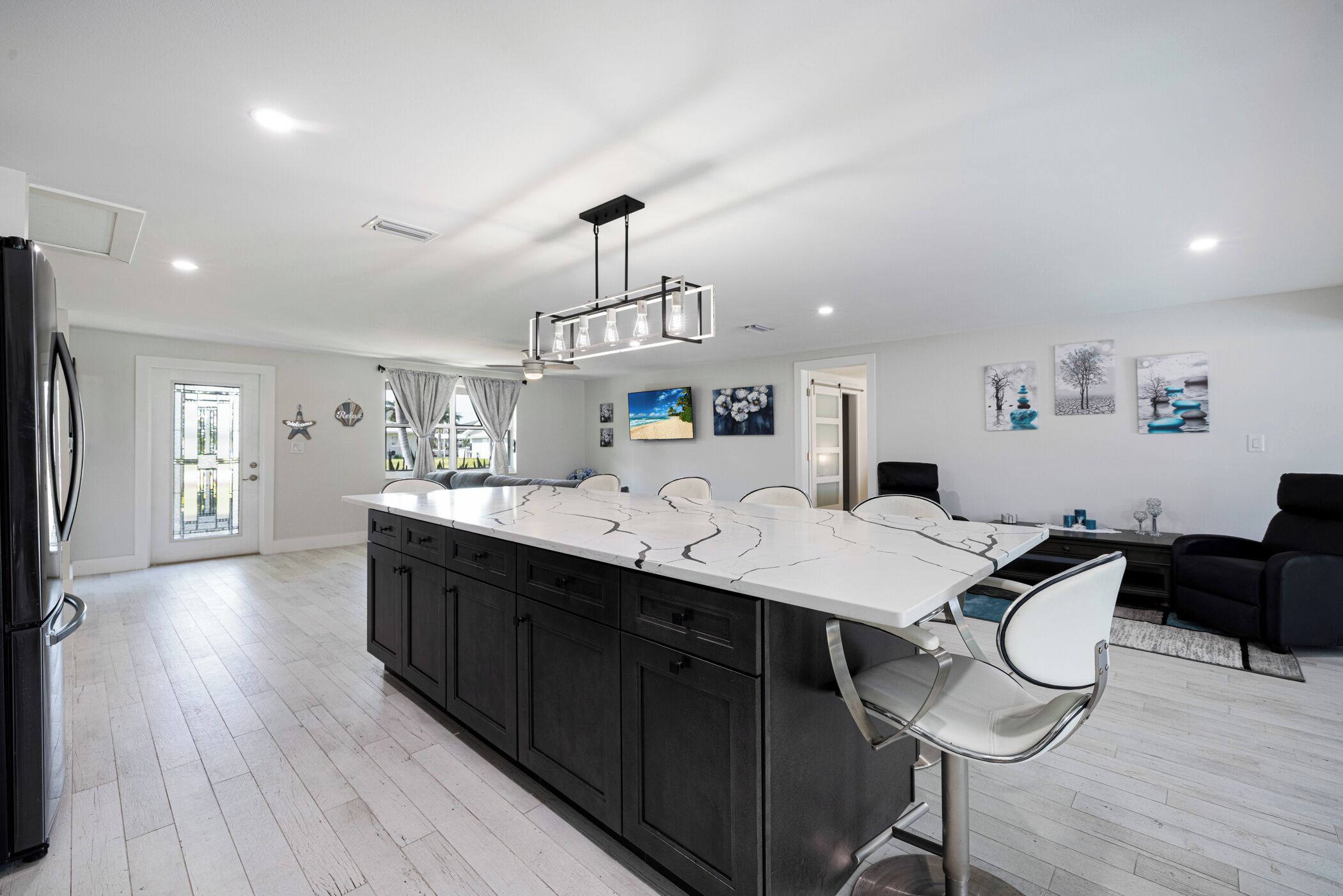 A modern kitchen with a large island, dark cabinets, and a stainless steel refrigerator.