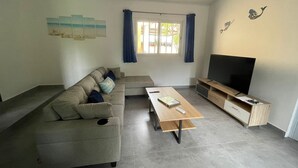 A living room with a sectional sofa, a coffee table, a flat-screen TV, and a window with curtains. - Casa Fofo (San Carlos)