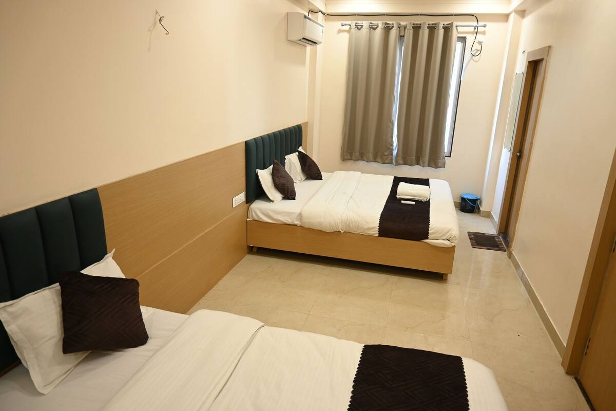 Habitación de hotel con dos camas, cabecera, ventana con cortinas y equipo de aire acondicionado.