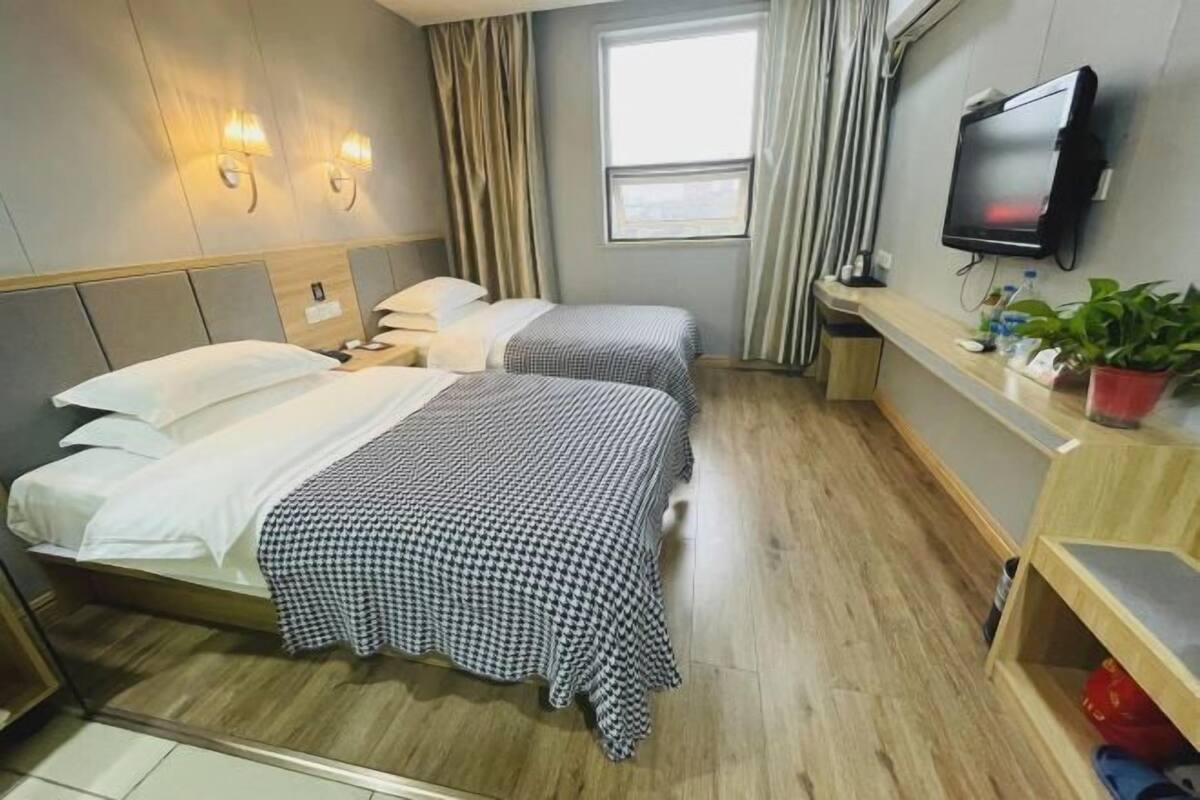 A hotel room with two beds, a TV, a small desk, and a window.
