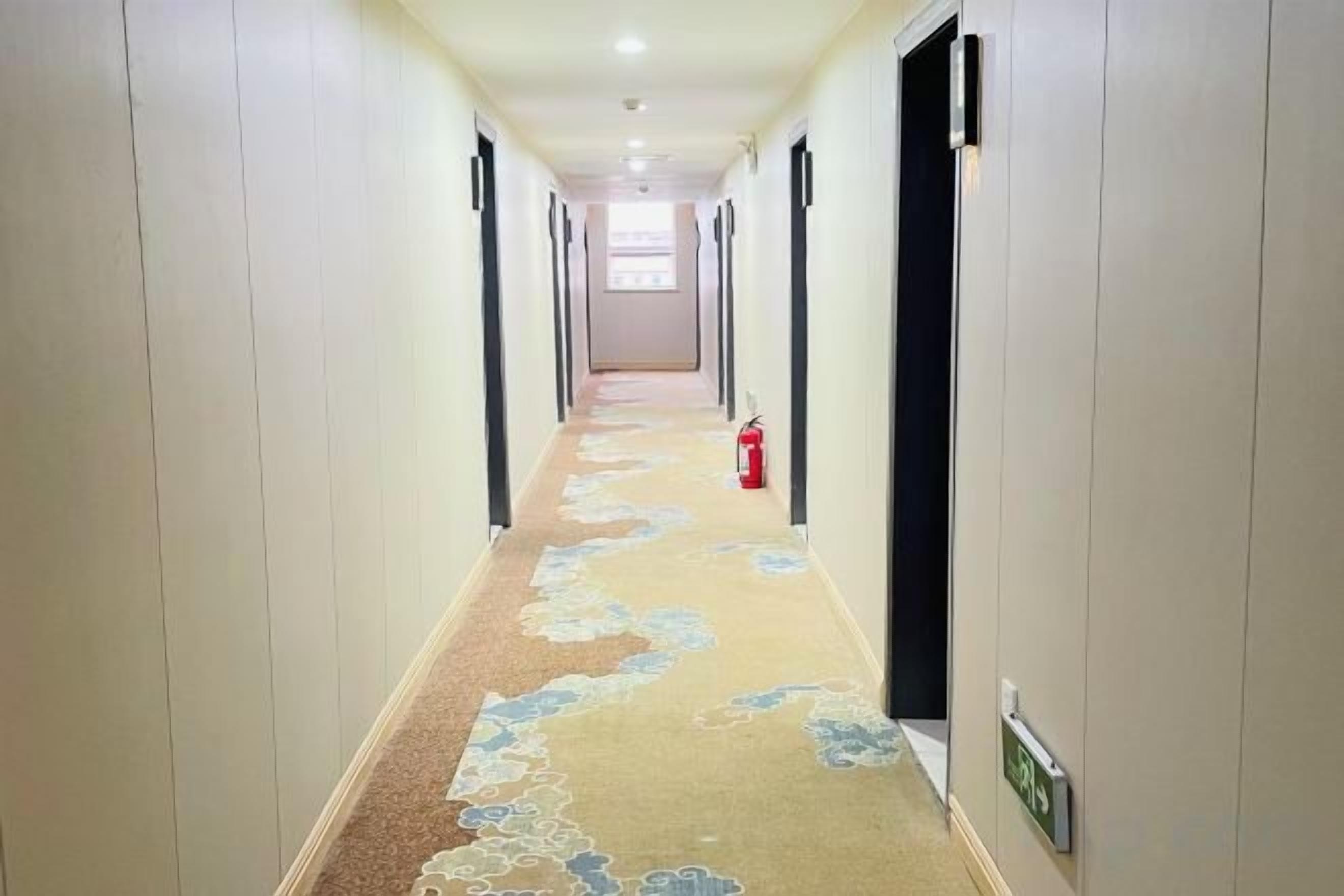 Un pasillo de hotel con un extintor, un reloj y una puerta a la derecha.