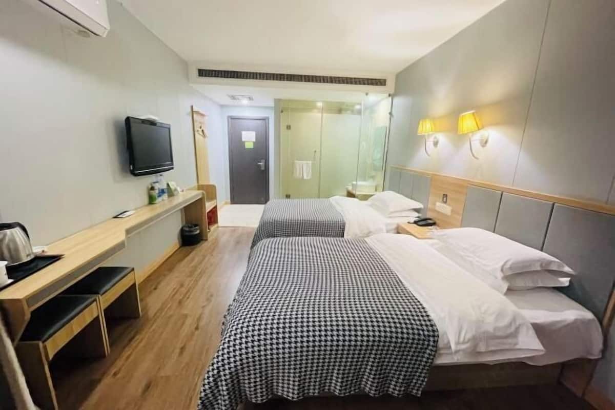 A hotel room with two beds, a desk, a TV, and a shower area.
