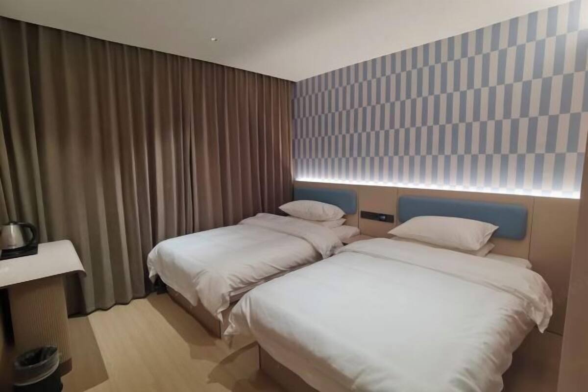 A hotel room with two beds, a desk, a trash bin, and a patterned wall.