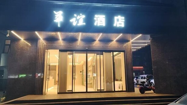 A hotel entrance with illuminated signage, a glass door, and a vehicle parked outside. - Huayi Commercial Hotel (Jiyuan)