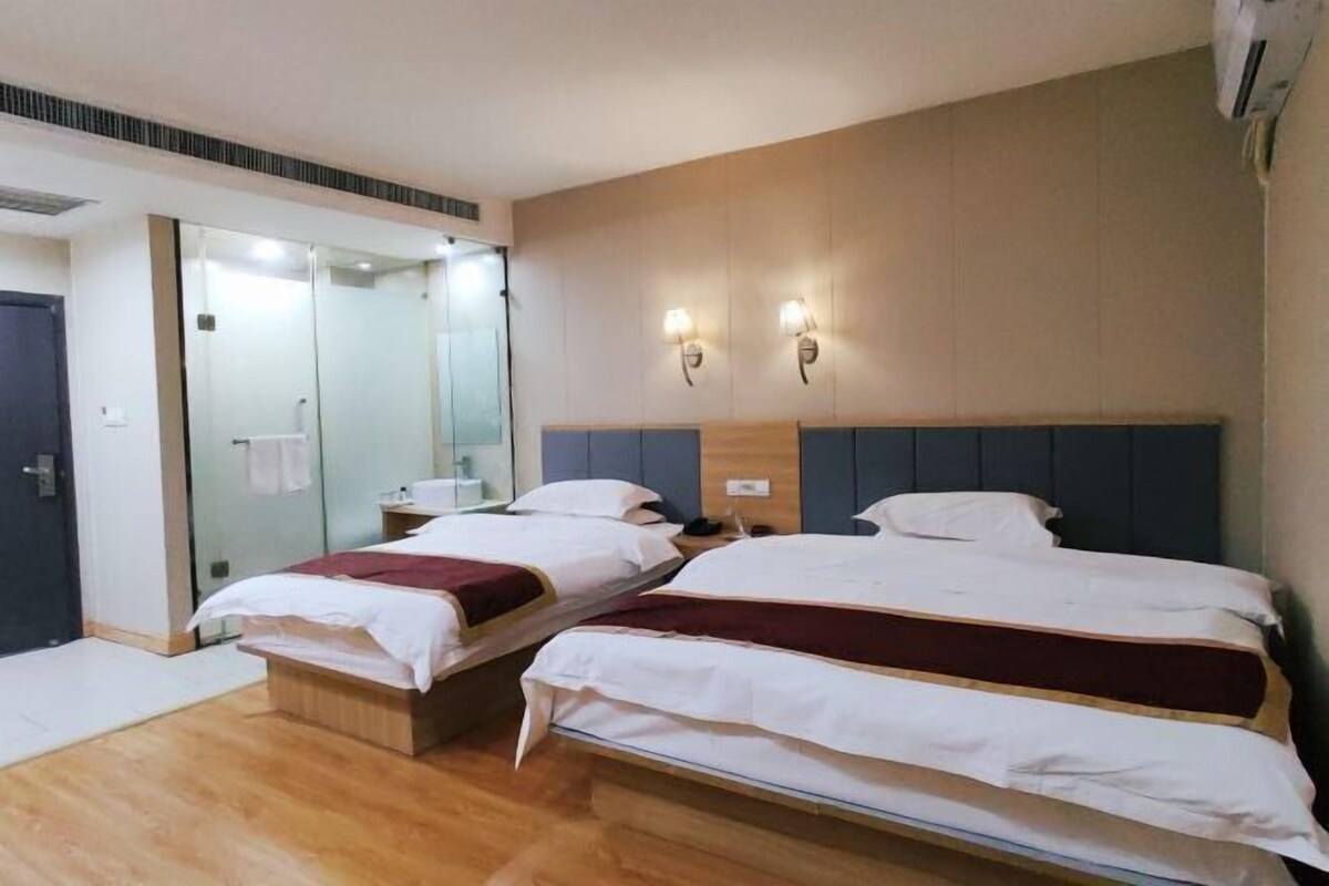 A hotel room with two beds, a mirror, a wooden headboard, and a wall-mounted light fixture.