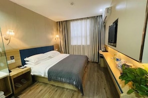 A hotel room with a bed, bedside table, lamp, and a TV mounted on the wall.