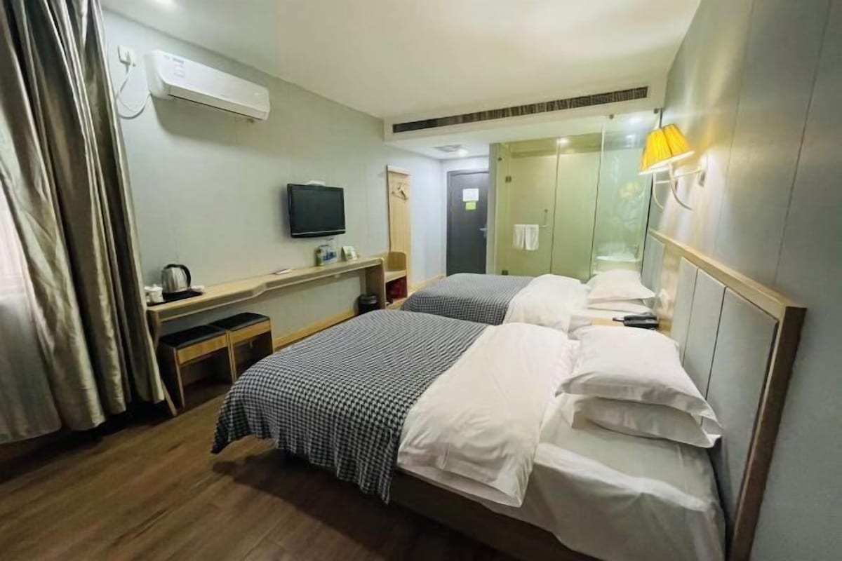 A hotel room with two beds, a desk, a television, and an air conditioning unit.