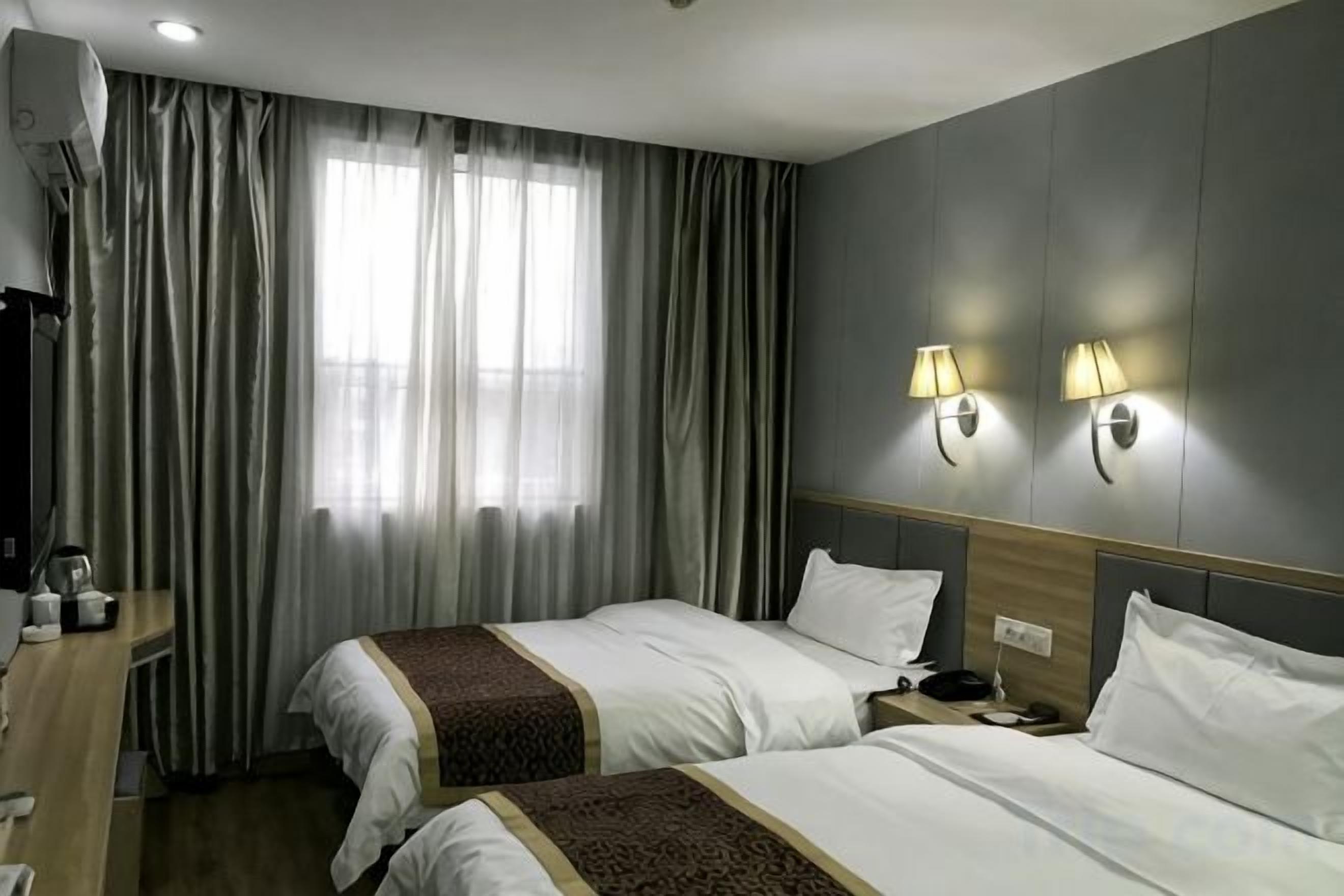 Habitación de hotel con dos camas, un escritorio con lámpara y una ventana con cortinas.