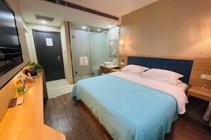 A hotel room with a bed, a bedside table, a mirror, a shower area, and a TV on a stand.