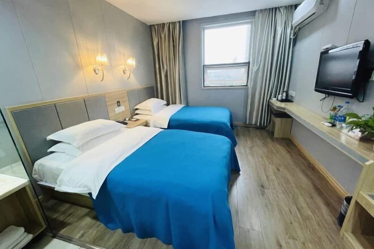 A hotel room with two beds, a TV, a window with curtains, and a desk with a plant.