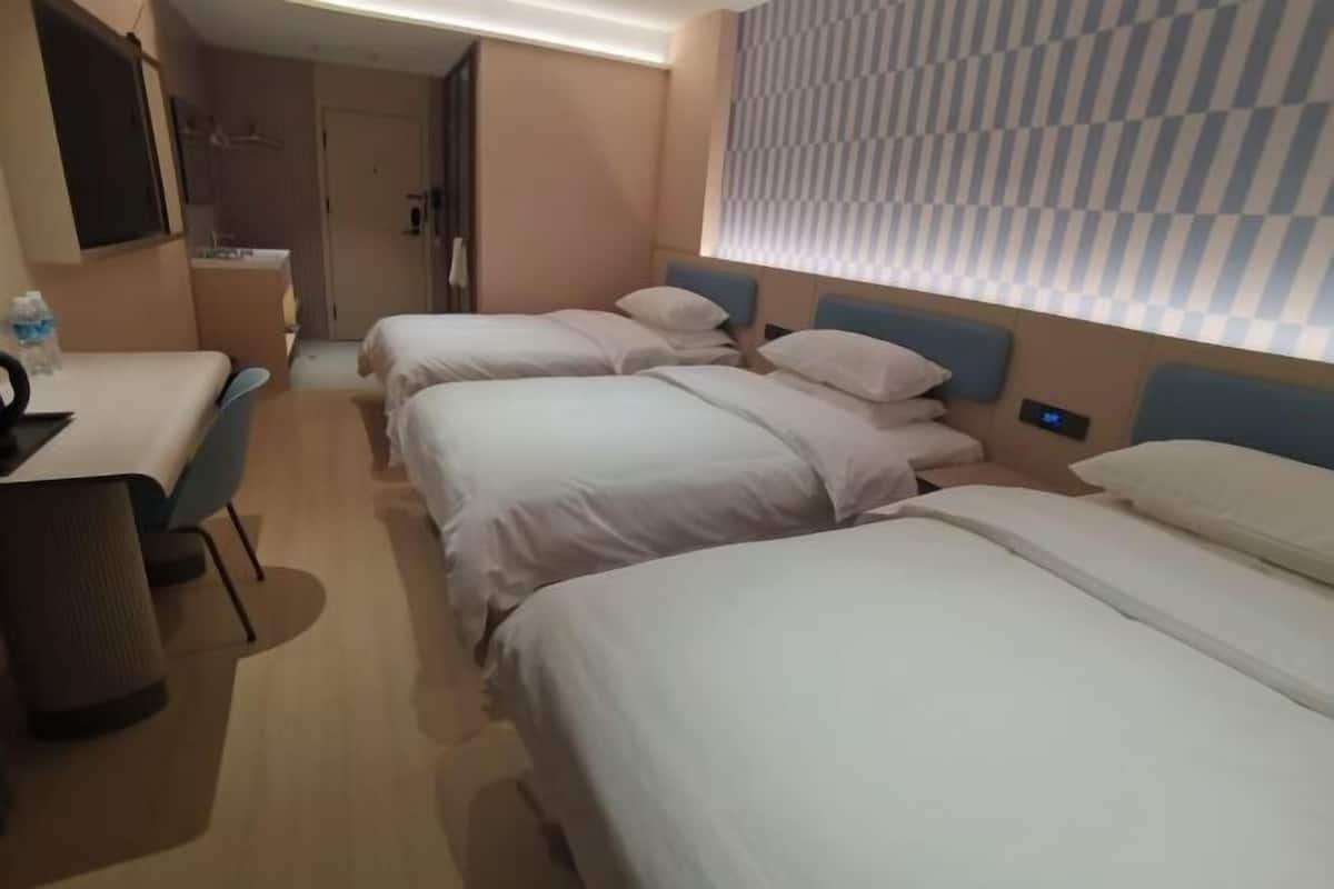 A hotel room with three single beds, a desk, and a chair.