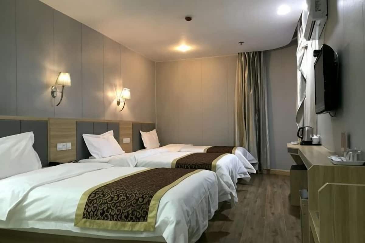 A hotel room with two beds, a desk with a chair, a flat-screen TV, and a window with curtains.