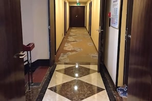 Un couloir d’hôtel avec un comptoir d’enregistrement, un panneau d’affichage et une porte au bout.