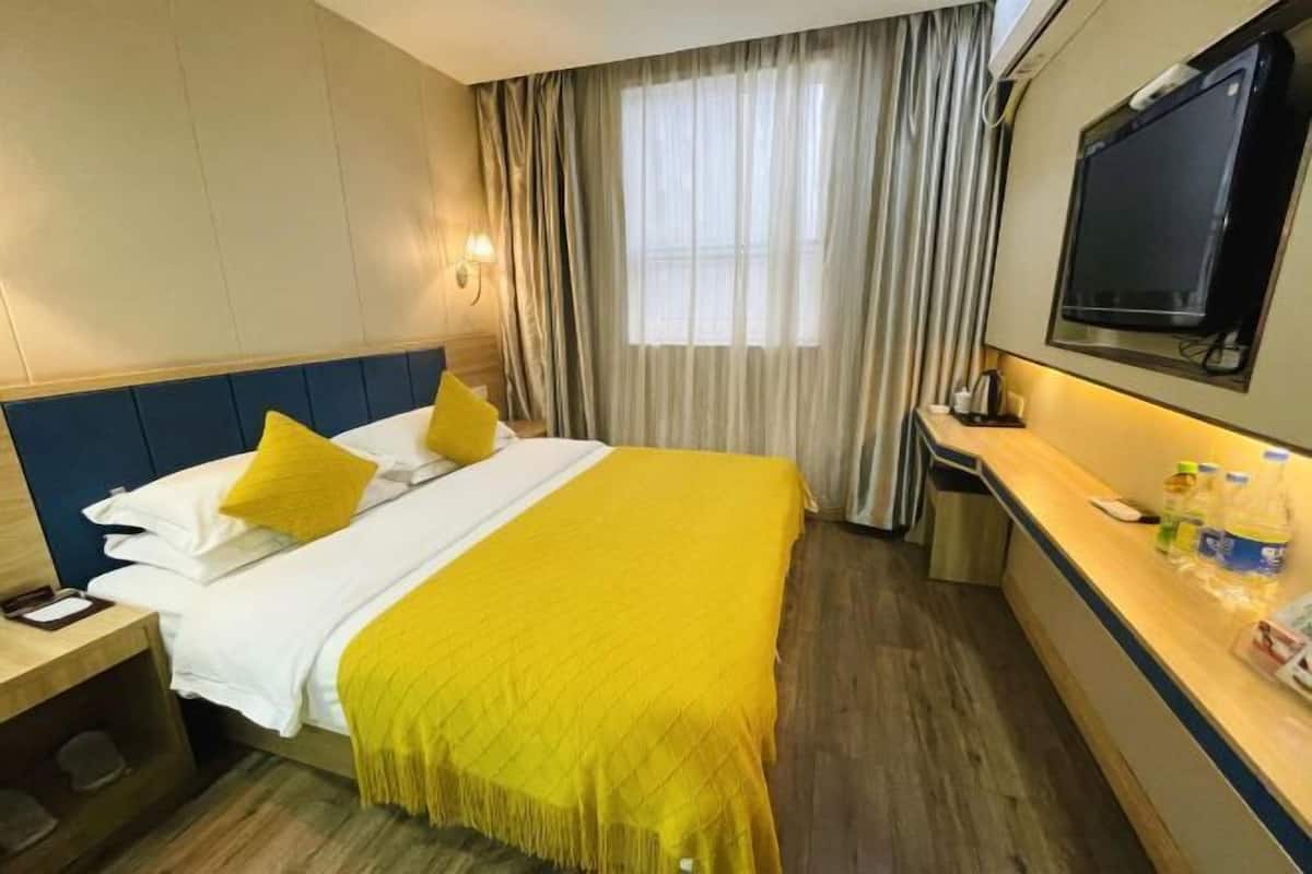 A hotel room with a bed, a desk, a television, and a window with curtains.