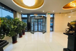 Un hall d’hôtel doté d’une porte tournante, de plantes en pot et d’un comptoir d’accueil.